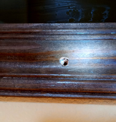 Close-up showing one of the two small holes in the bottom of the wooden frame of the Guinness mirror